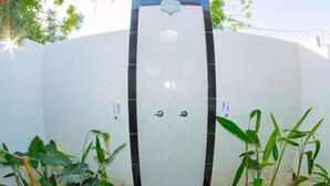 A modern bathroom with a white and black tiled wall, a shower area, and potted plants around the entrance. - The Villa Dini Dnusa Lembongan (Lembongan Island)