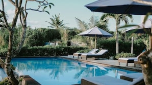 A swimming pool with lounge chairs and umbrellas, surrounded by lush greenery. - The Villa Dini Dnusa Lembongan (Lembongan Island)