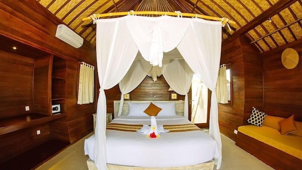 A four-poster canopy bed with a white canopy, a wooden headboard, and a small decorative bird on the bed. - The Villa Dini Dnusa Lembongan (Lembongan Island)