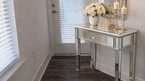 A hallway with a white door, a mirror, a console table with a vase of white flowers, and two candles.