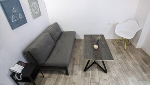 A modern living room with a grey sofa, a small wooden table with a vase, and a white chair with gold legs. - Athensotel.com (Athens)
