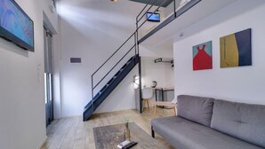 A modern living room with a grey sofa, a coffee table, a TV, and a staircase. - Athensotel.com (Athens)