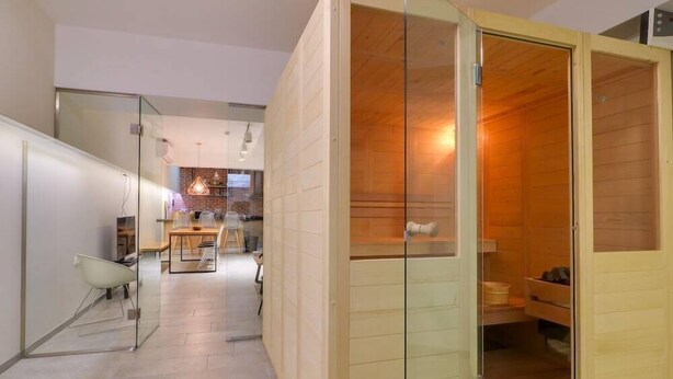 A modern interior with a sauna, a glass-walled seating area, and a kitchen in the background. - Athensotel.com (Athens)