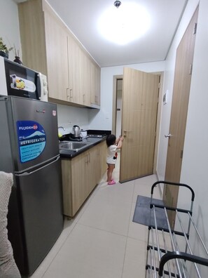 A compact kitchen with a refrigerator, a kettle, and wooden cabinets. - Gvsky suite Moa Staycation (Pasay City)