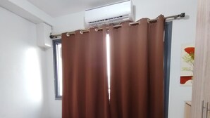 Et soveværelse med seng, aircondition, et vindue med gardiner og et skab.