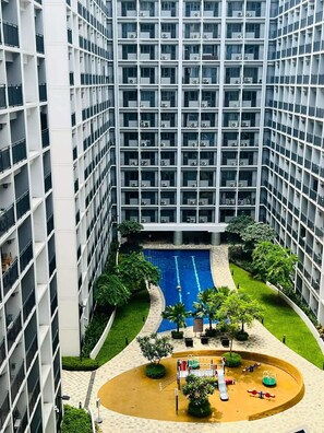 A high-rise building with multiple balconies, a central swimming pool, and a playground area. - Gvsky suite Moa Staycation (Pasay City)