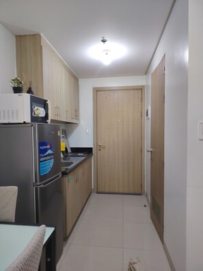 A compact kitchen with a refrigerator, microwave, and wooden cabinets. - Gvsky suite Moa Staycation (Pasay City)