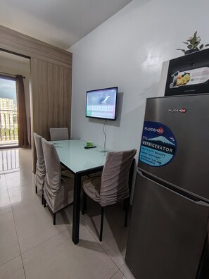A hotel room with a dining table, chairs, a television mounted on the wall, and a refrigerator. - Gvsky suite Moa Staycation (Pasay City)