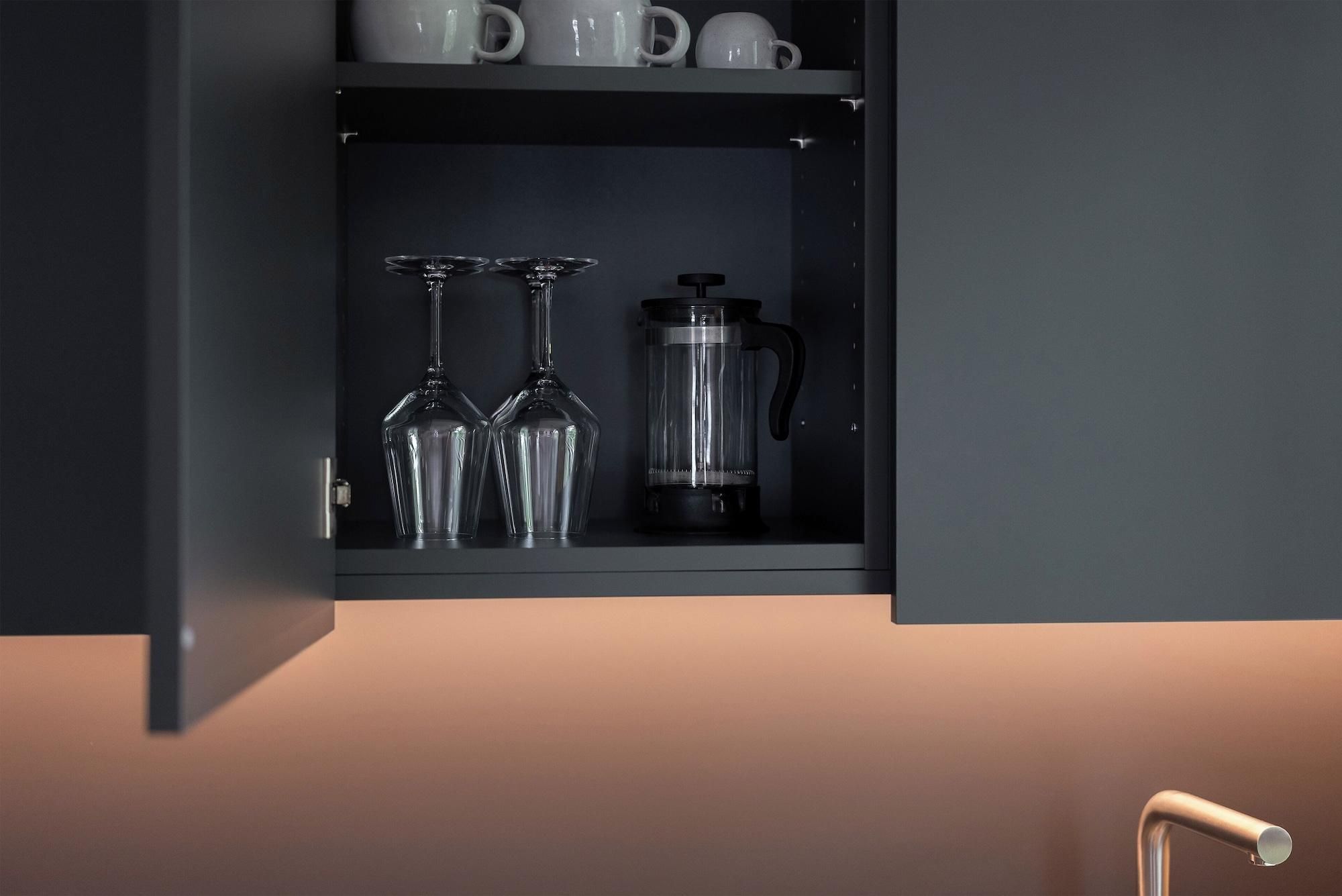 Een keukenkastje met een koffiezetapparaat, twee wijnglazen en verschillende mokken.