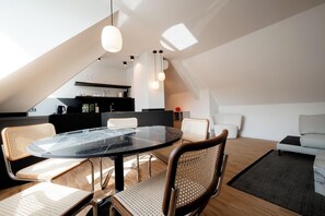 Un moderno loft con angolo ristoro con tavolo in vetro e sedie in rattan, cucina con mobili scuri e zona living con divano e tavolino.