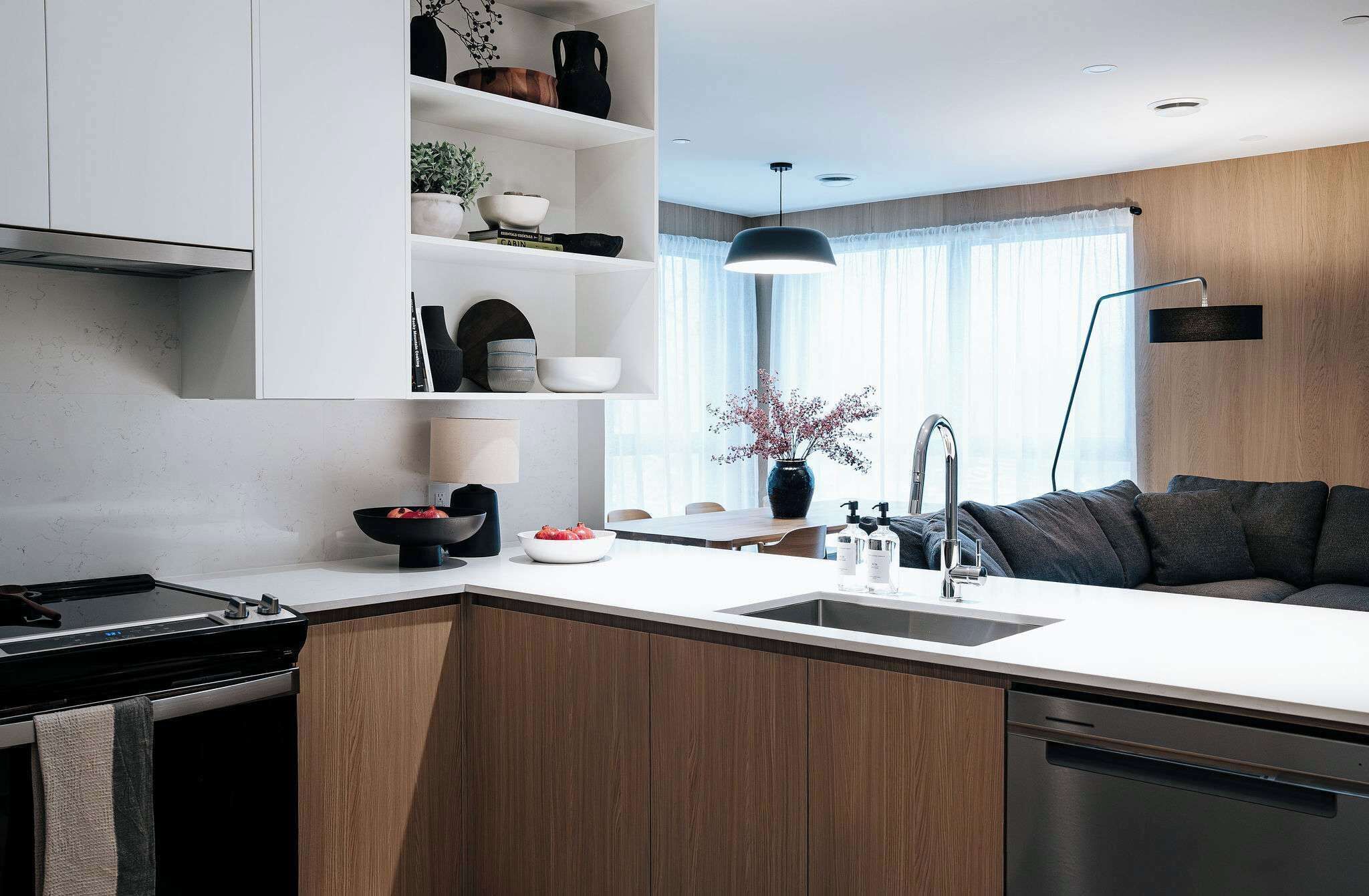 A modern kitchen with a central island, built-in shelves, a dining area, and a dark-colored sofa.