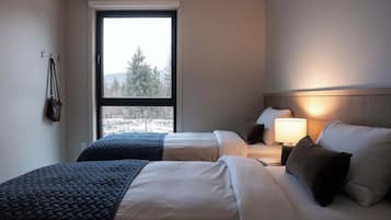 A hotel room with two beds, a window with a view of trees, a lamp on the nightstand, and a coat rack with a bag.