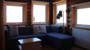 Accogliente camera in una casetta di legno con divano componibile, un piccolo tavolo in legno e tre finestre che lasciano entrare luce naturale.