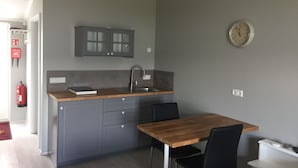 Een compacte keuken met grijze kastjes, een houten aanrechtblad en een klok aan de muur.