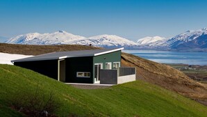 A modern house with a flat roof, a small porch, and a view of snow-capped mountains and a lake. - Hrimland (Akureyri)