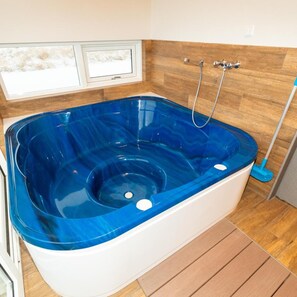 A modern bathroom with a large blue jacuzzi tub, wooden floor, and a window with a view. - Hrimland (Akureyri)