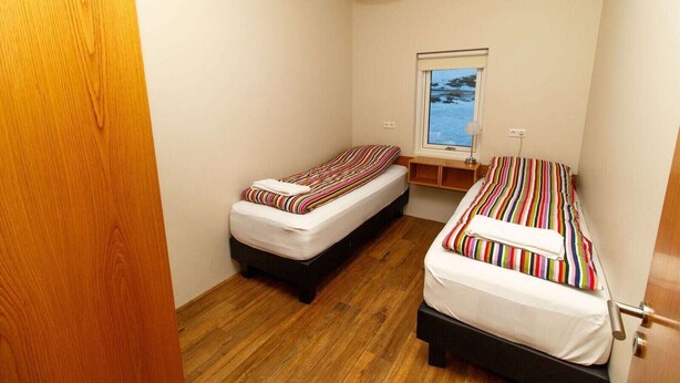 A small, compact room with two single beds, a window with a view, and a wooden floor. - Hrimland (Akureyri)