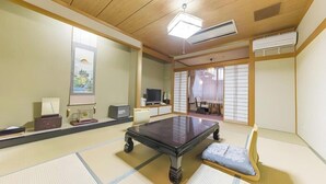 Een traditionele Japanse kamer met tatami vloeren, een lage tafel, een zachte stoel, een televisie en schuifdeuren.