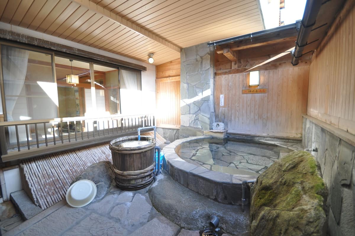 Un interior de madera con una bañera de hidromasaje de piedra, vigas de madera y una pared de piedra.