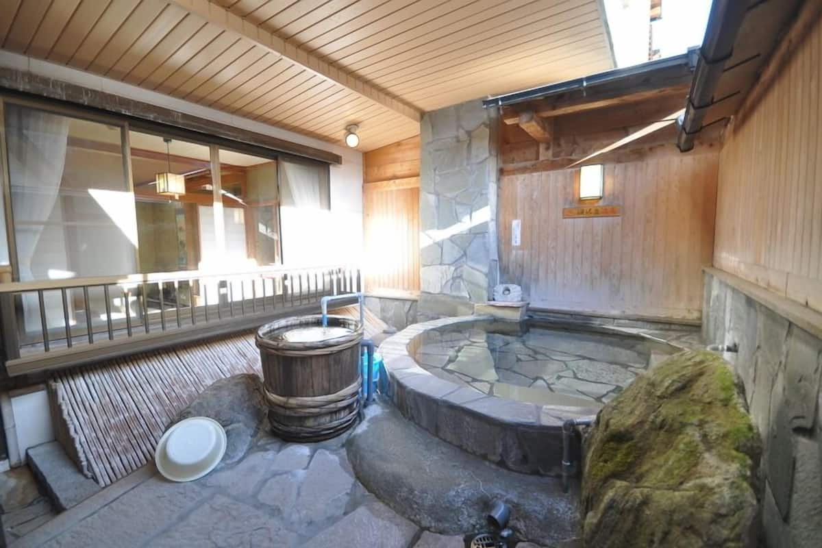 Un área de aguas termales con suelo de piedra, bancos de madera y una valla de madera.