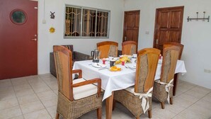 Een eetgedeelte met een ronde tafel voor vier personen, omringd door rieten stoelen met witte kussens.