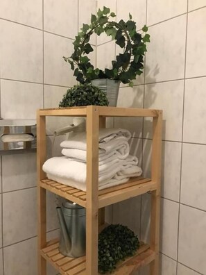 A wooden shelf with folded towels and a potted plant in a bathroom with tiled walls. - Hamburg Room (Hamburg)
