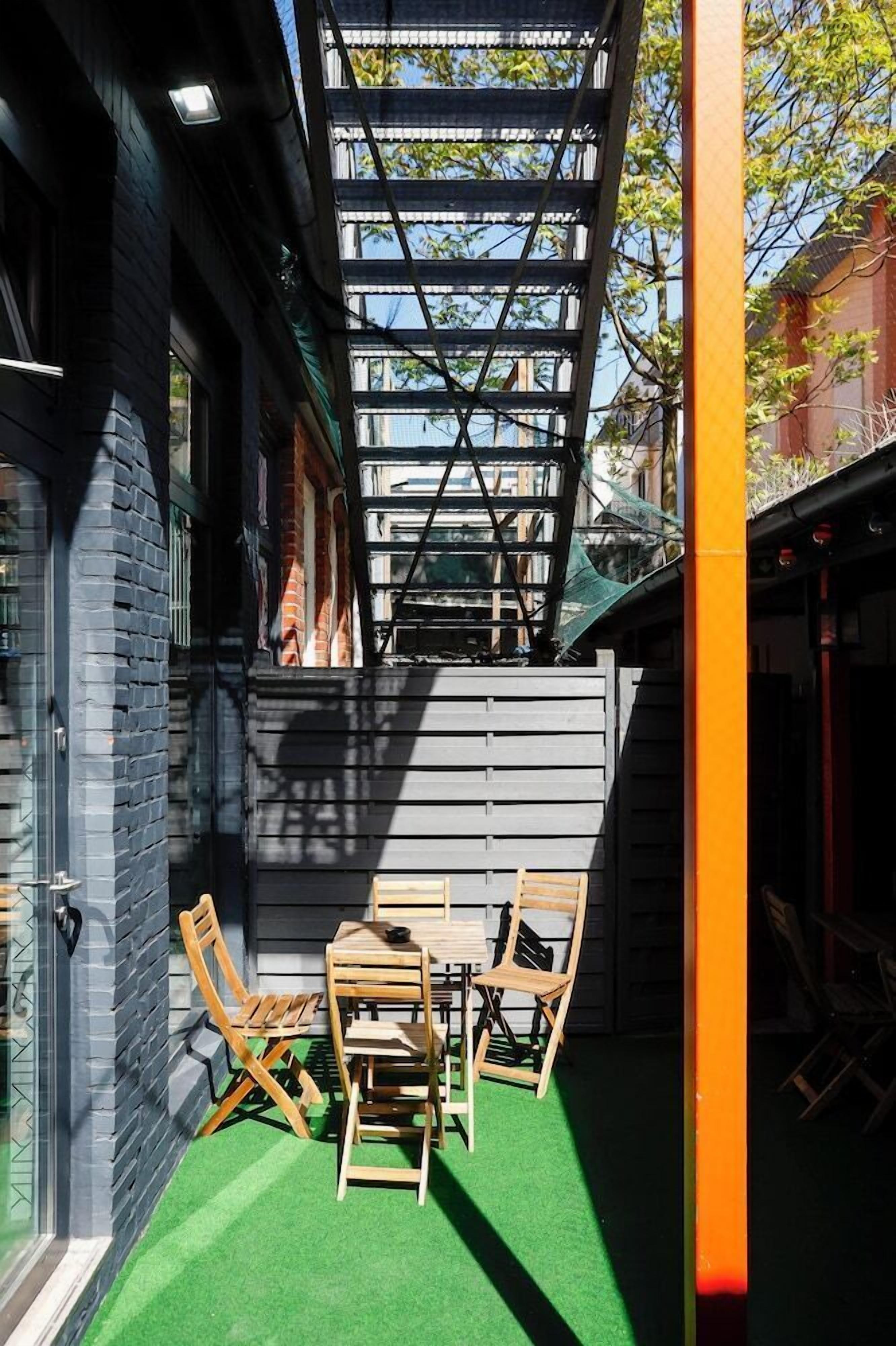 A patio with a wooden table and chairs, a green artificial turf floor, and a metal pergola structure.