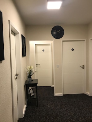 Ein Flur mit zwei weißen Türen, einer schwarzen Uhr und einem kleinen Tisch mit einer Pflanze.