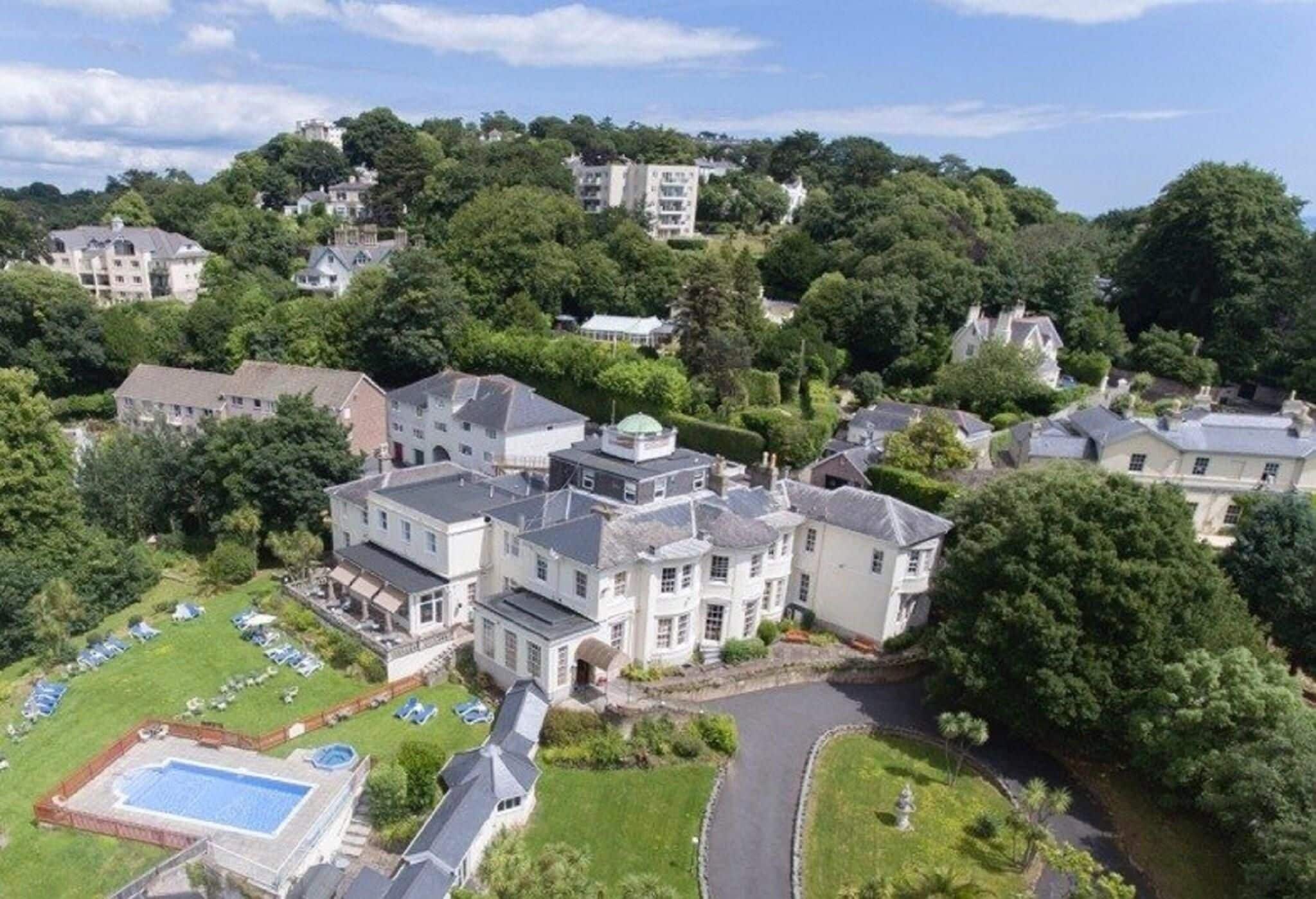 A large, multi-story building with a swimming pool, surrounded by lush greenery and other residential buildings.