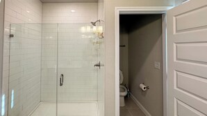 Ein modernes Badezimmer mit einer gläsernen Duschkabine, weißen Fliesenwänden und einem beigen Boden.