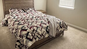 Ein Schlafzimmer mit einem hölzernen Bettgestell, einer gemusterten Bettdecke und einem Fenster mit Jalousien.