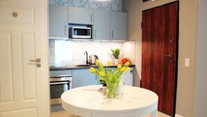 A kitchen with a white table, four stools, a microwave, an oven, and a door with a wooden panel. - Jessapart Hotel - Triton Park (Warsaw)