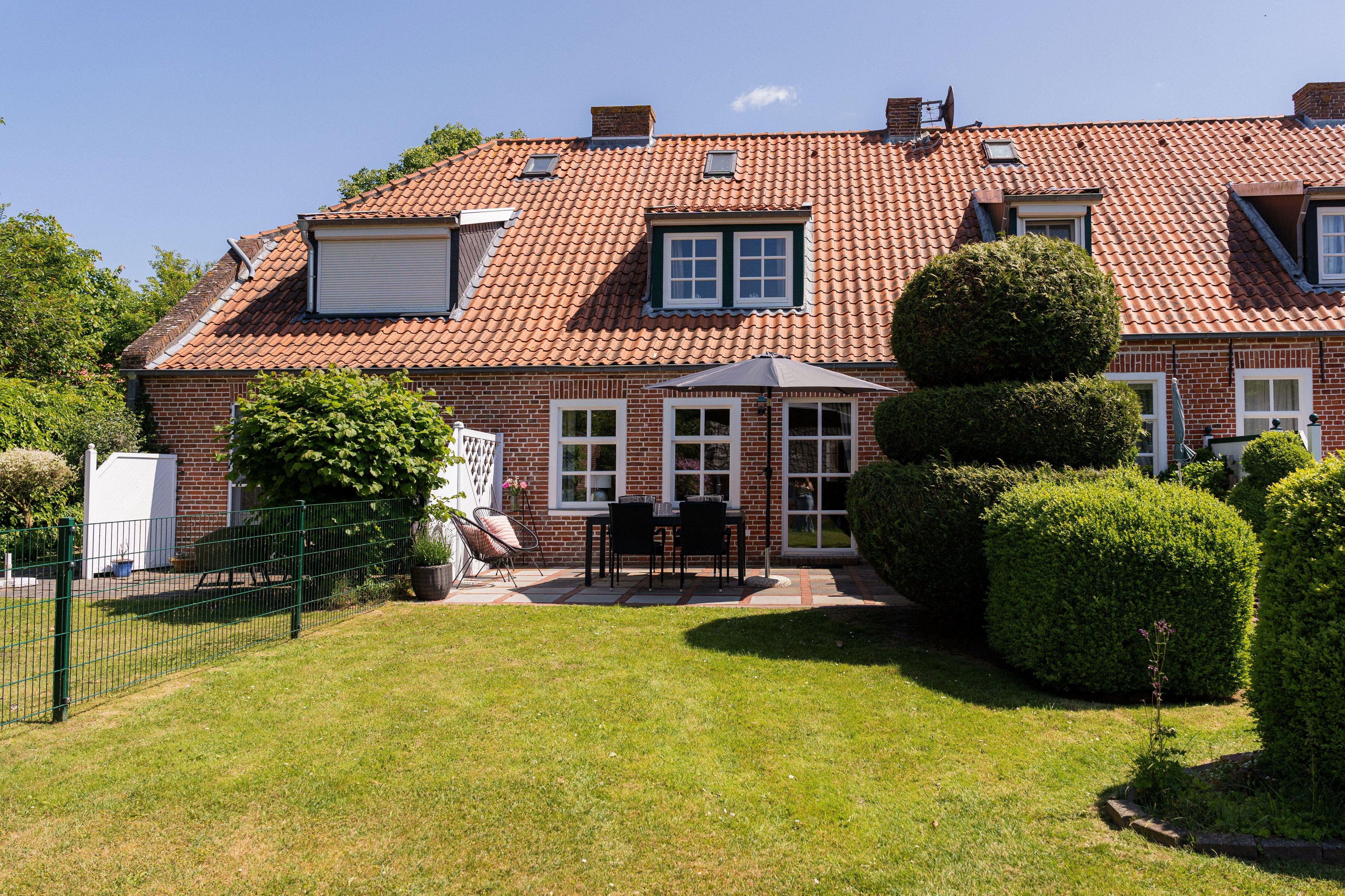 A two-story house with a red-tiled roof, a fenced backyard, and a patio with outdoor furniture.