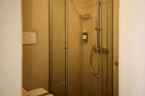 Un box de ducha con paredes de vidrio, un cabezal de ducha manual y un grifo en la pared.
