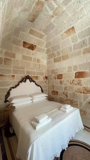 Een kamer met een stenen muur, een bed met witte lakens en een houten hoofdeinde.