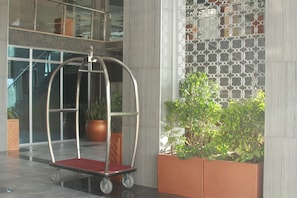 Um hall com um carrinho de metal, plantas em vasos e uma parede estampada.