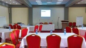 Sala de conferência com mesas, cadeiras, um púlpito e um projetor.