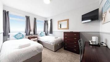 Quarto de hotel com duas camas, cômoda, escrivaninha, televisão e janela com cortinas.