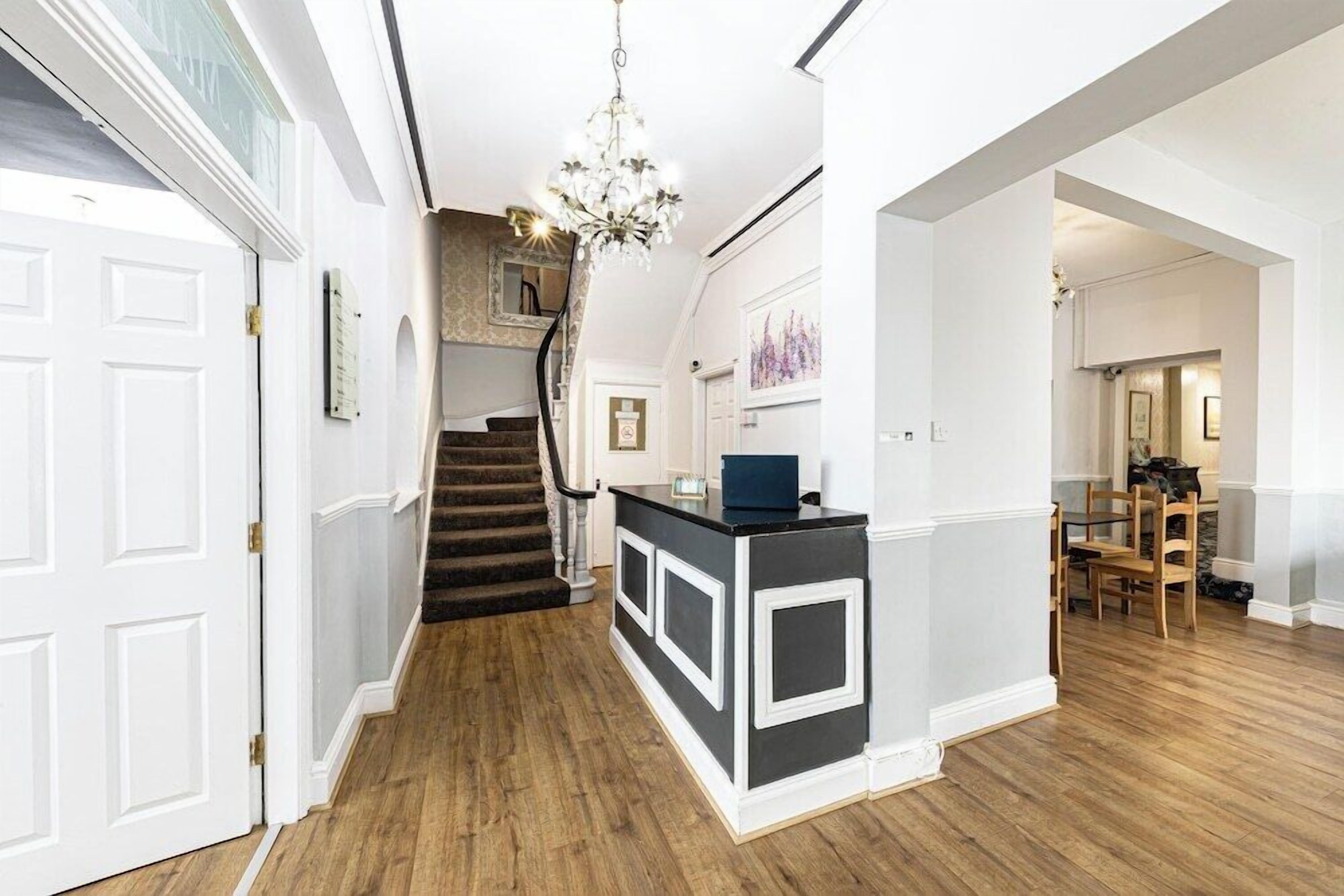 Um corredor com escadaria, balcão de recepção e sala de jantar com cadeiras e mesa de madeira.