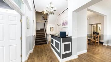 Um corredor com escadaria, balcão de recepção e sala de jantar com cadeiras e mesa de madeira.