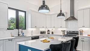 Una cocina moderna con armarios blancos, una isla azul, sillas negras e iluminación colgante.
