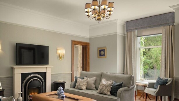 A living room with a grey sofa, a coffee table, a fireplace, a television, and a large window with curtains. - The Marcliffe Hotel And Spa (Aberdeen)