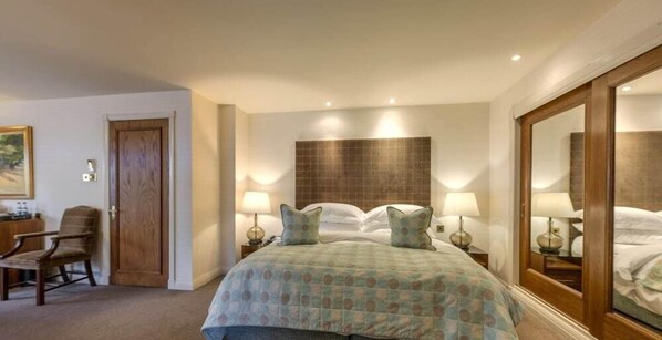 Une chambre d’hôtel avec un grand lit, deux lampes de chevet, une chaise en bois et un grand miroir.