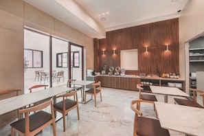 A modern dining area with marble flooring, wooden tables and chairs, a central counter with decorative items, and a view through large windows. - Piano Hotel (Daegu)