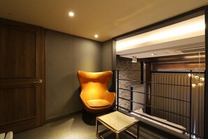 Een moderne badkamer met een houten deur, een bijzondere oranje stoel, een glazen tafeltje en een douchegedeelte met een glazen scherm.