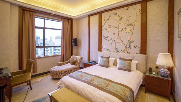 Habitación de hotel con una cama grande, un escritorio, una silla, un ventanal con vista a la ciudad y un adorno en la pared.