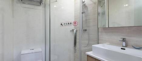 A modern bathroom with a glass-enclosed shower, a white toilet, and a sink with a mirror above it.