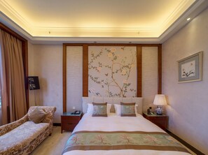 Habitación de hotel con una cama grande, un sofá, una mesita de noche, una lámpara y un cuadro en la pared.