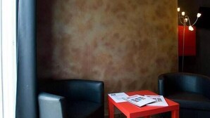 A room with a large wall, two black chairs, a red table, and a floor lamp. - Hospedería Almundo (Tarifa)