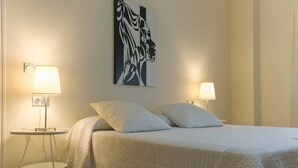 A neatly made bed with two pillows, a bedside lamp, and a wall-mounted artwork. - Hospedería Almundo (Tarifa)
